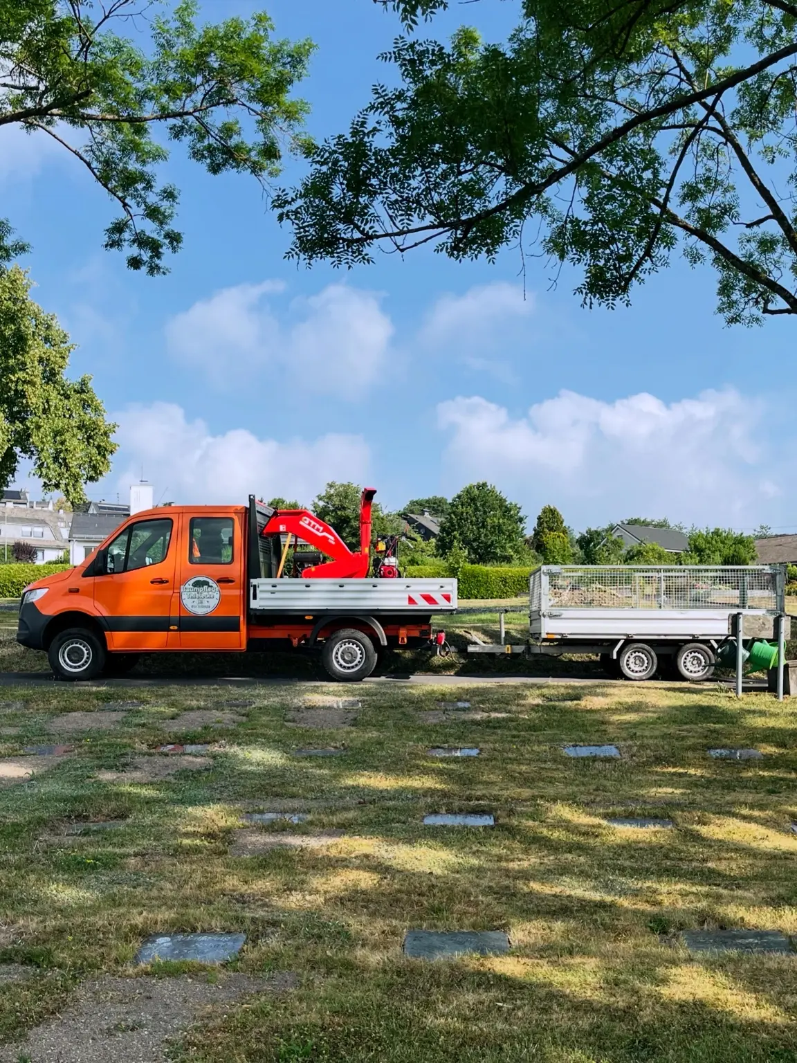 Orangefarbener Betriebswagen von Baumpflege Thielecke mit Häcksler und Anhänger