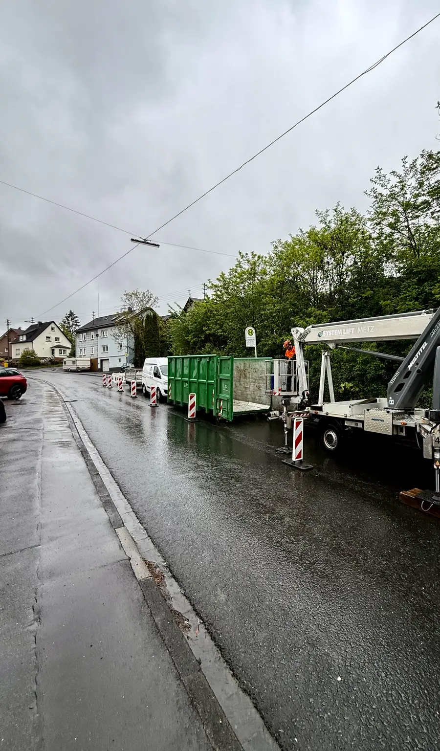 Abgesicherter Arbeitsbereich mit Hubarbeitsbühne und Mulde auf einer nassen Straße